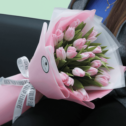 Soft pink tulip bouquet with fresh green foliage in elegant pink and white wrapping.
