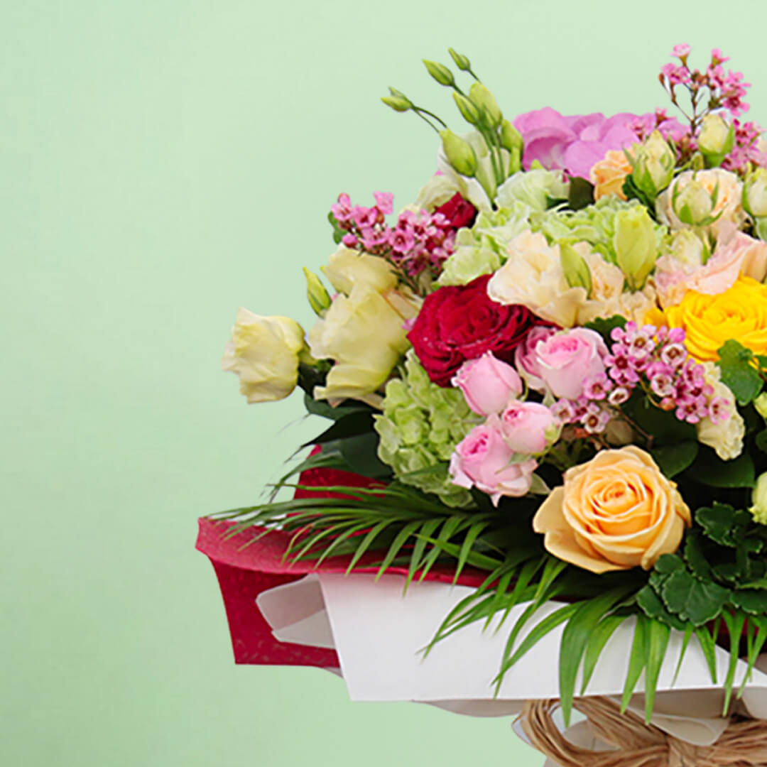 Mixed pink, cream, yellow and red roses with wax flowers, palm foliage and natural jute wrapping