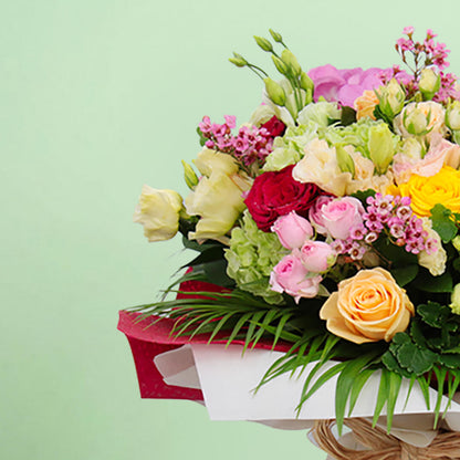 Mixed pink, cream, yellow and red roses with wax flowers, palm foliage and natural jute wrapping