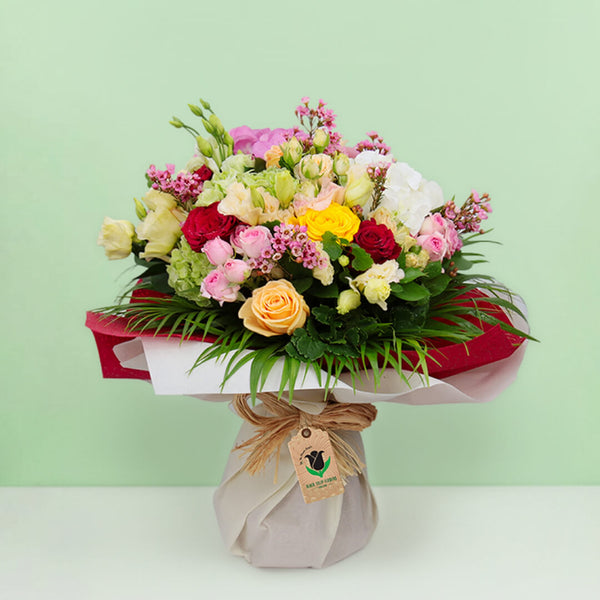 Mixed pink, cream, yellow and red roses with wax flowers, palm foliage and natural jute wrapping