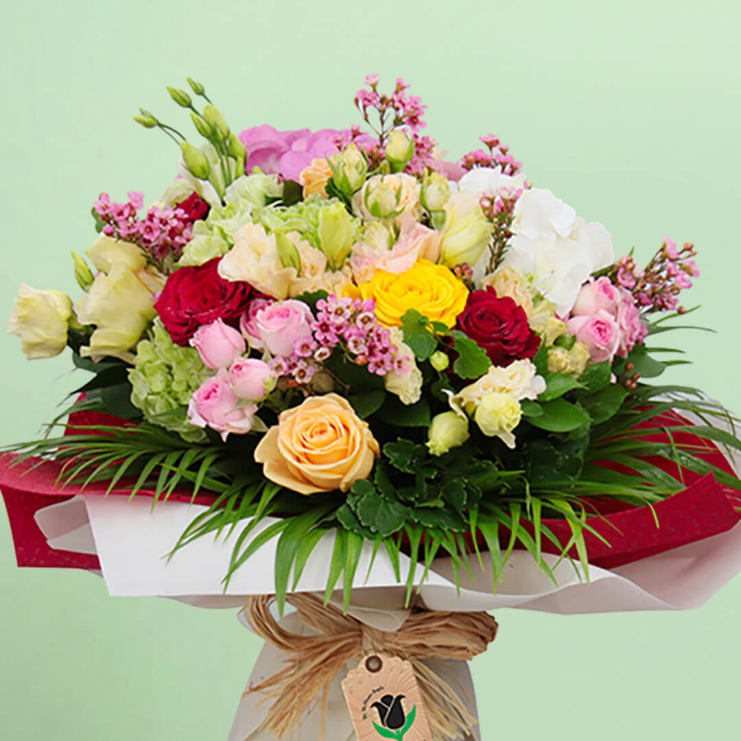 Mixed pink, cream, yellow and red roses with wax flowers, palm foliage and natural jute wrapping
