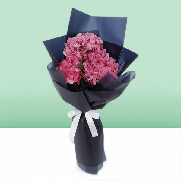 Dark pink hydrangea bouquet wrapped in navy non-woven paper with a white ribbon
