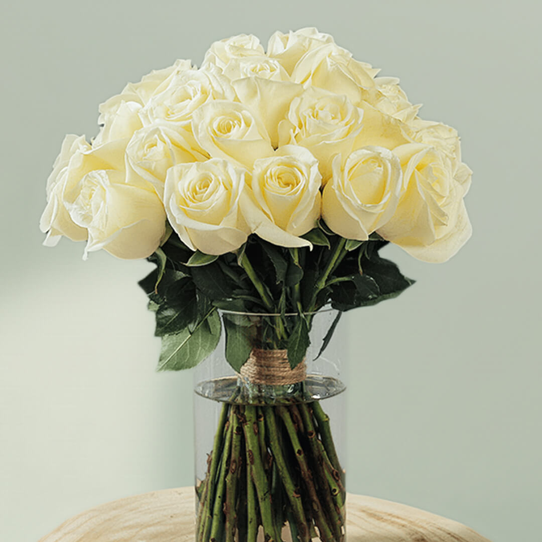30 fresh white roses with vibrant green foliage are elegantly arranged in a transparent cylinder glass vase.