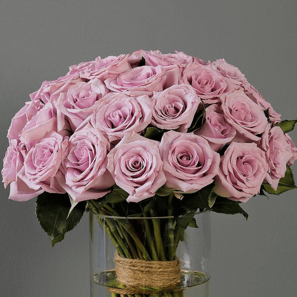 Fresh purple roses and vibrant foliage are beautifully styled in a transparent cylinder glass vase