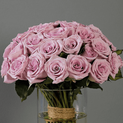 Fresh purple roses and vibrant foliage are beautifully styled in a transparent cylinder glass vase