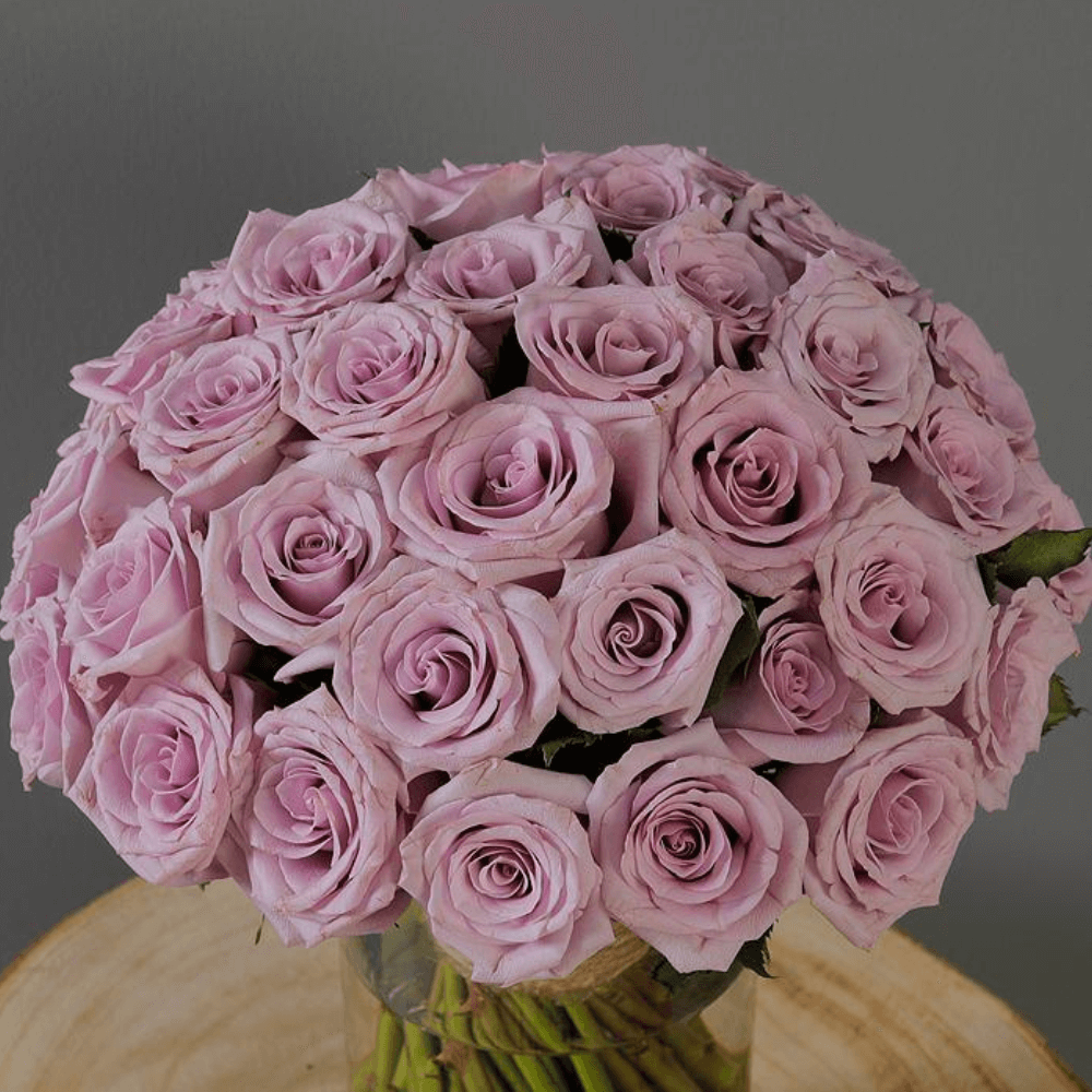 Fresh purple roses and vibrant foliage are beautifully styled in a transparent cylinder glass vase