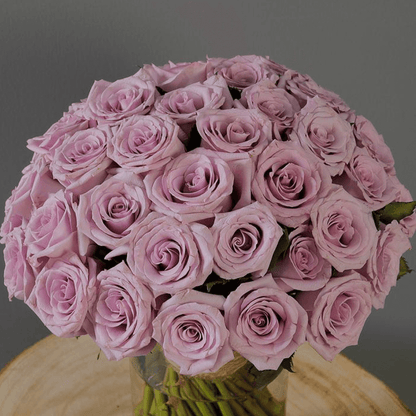 Fresh purple roses and vibrant foliage are beautifully styled in a transparent cylinder glass vase