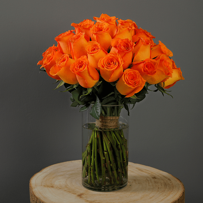 A glass vase arrangement with orange roses and green foliage.