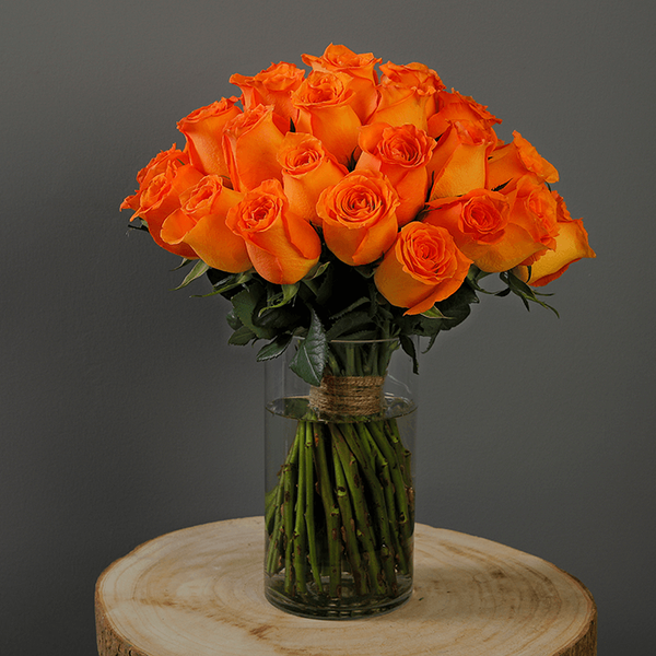 A glass vase arrangement with orange roses and green foliage.