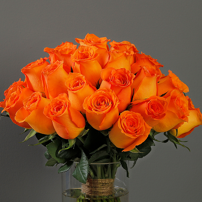 A glass vase arrangement with orange roses and green foliage.