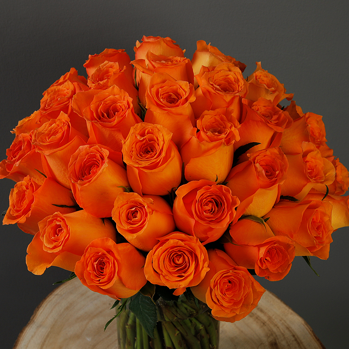 A glass vase arrangement with orange roses and green foliage.