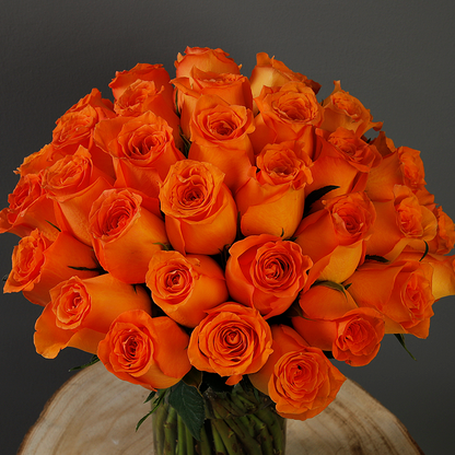 A glass vase arrangement with orange roses and green foliage.
