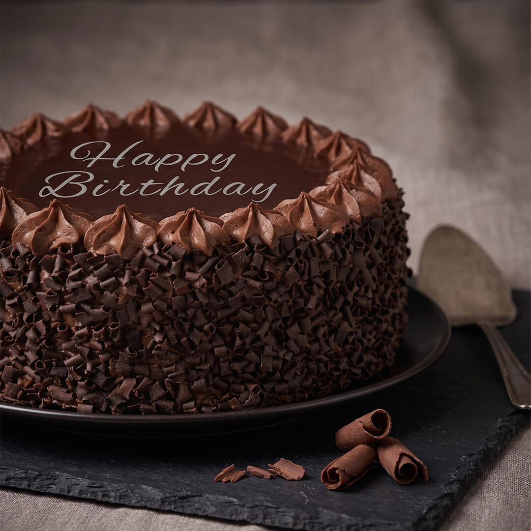 Chocolate truffle cake featuring smooth chocolate ganache, piped frosting, fresh berries and decorative chocolate pieces.
