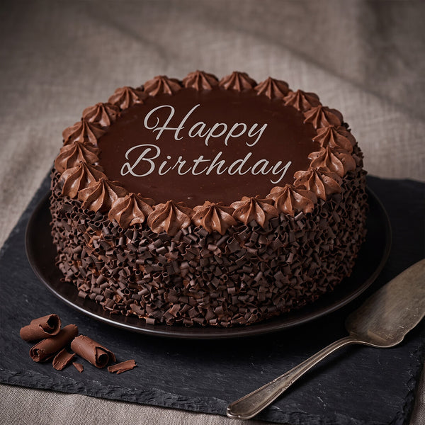Chocolate truffle cake featuring smooth chocolate ganache, piped frosting, fresh berries and decorative chocolate pieces.