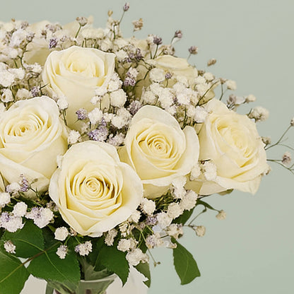20 white roses with gypsophila arranged in a cylindrical glass vase.