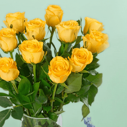 Vase arrangement with 20 yellow roses and fresh greenery in a transparent cylinder glass vase.