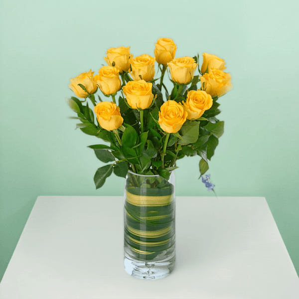 Vase arrangement with 20 yellow roses and fresh greenery in a transparent cylinder glass vase.