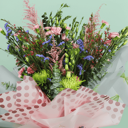 A pink bouquet of disbuds, spray roses, Eustoma, statice and astilbe with greenery in pink Korean-style flower sheets