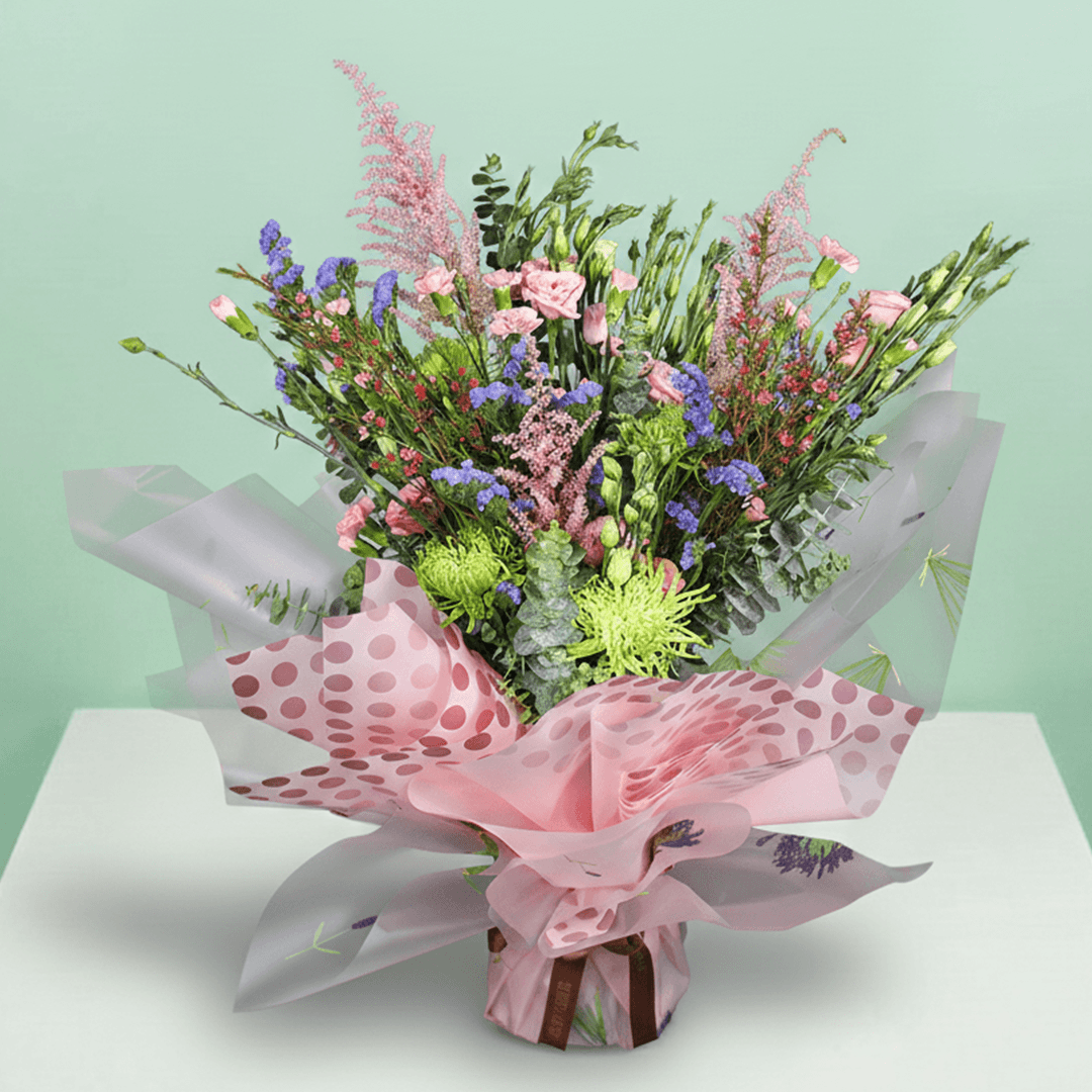 A pink bouquet of disbuds, spray roses, Eustoma, statice and astilbe with greenery in pink Korean-style flower sheets