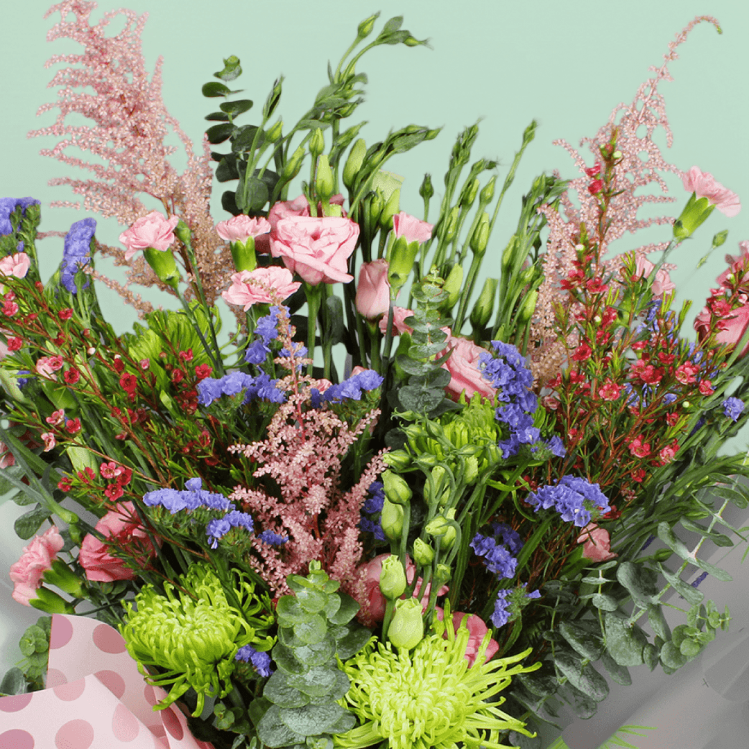 A pink bouquet of disbuds, spray roses, Eustoma, statice and astilbe with greenery in pink Korean-style flower sheets