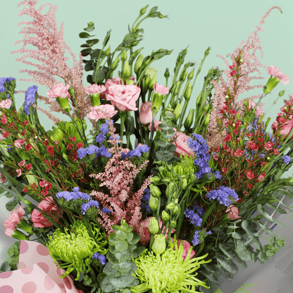 A pink bouquet of disbuds, spray roses, Eustoma, statice and astilbe with greenery in pink Korean-style flower sheets