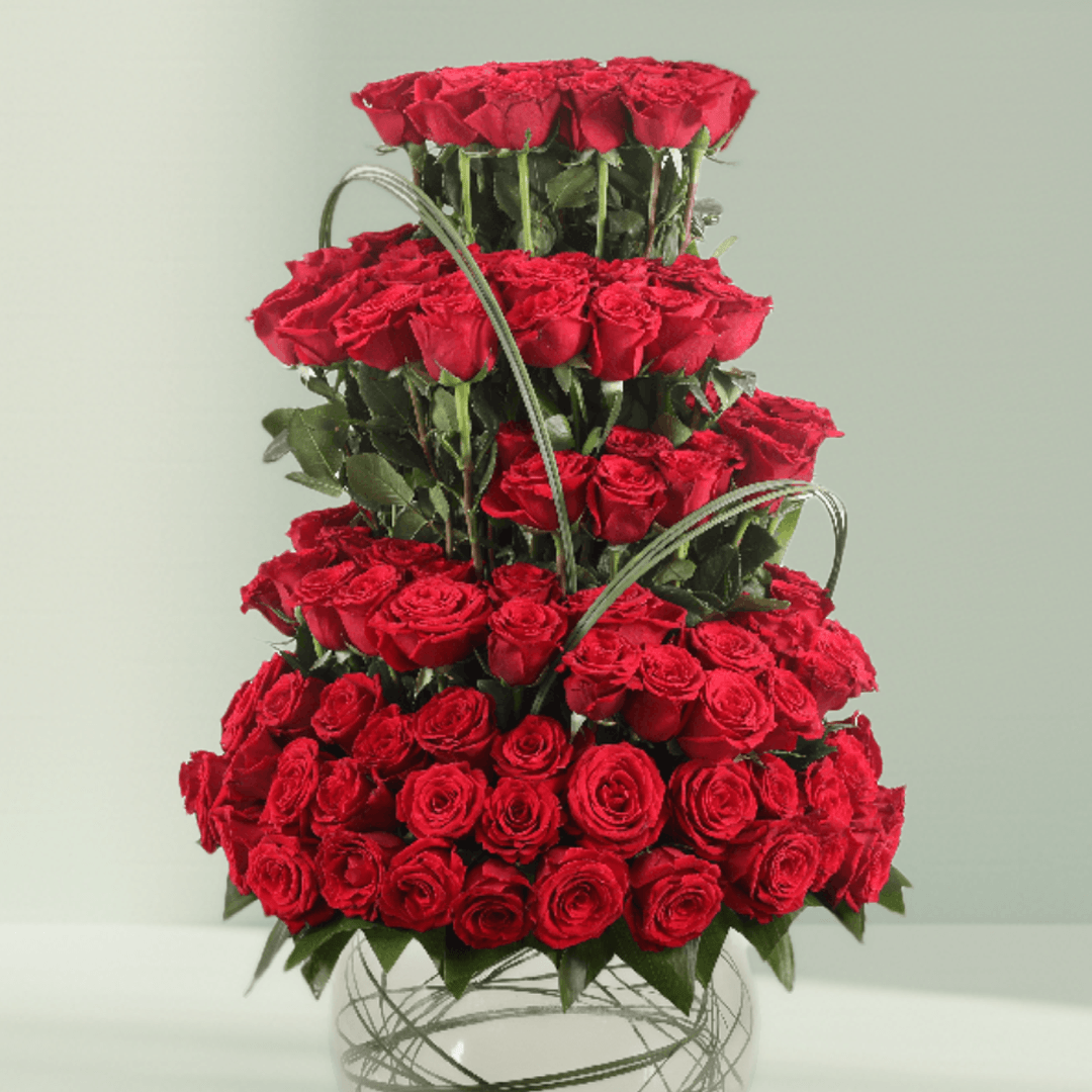 Multi-tier arrangement of 101 red roses with greenery in a transparent glass fishbowl vase