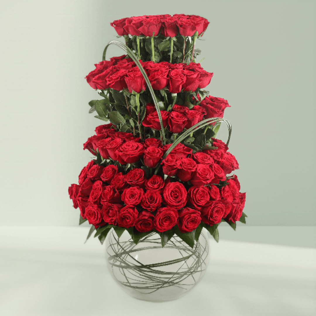 Multi-tier arrangement of 101 red roses with greenery in a transparent glass fishbowl vase