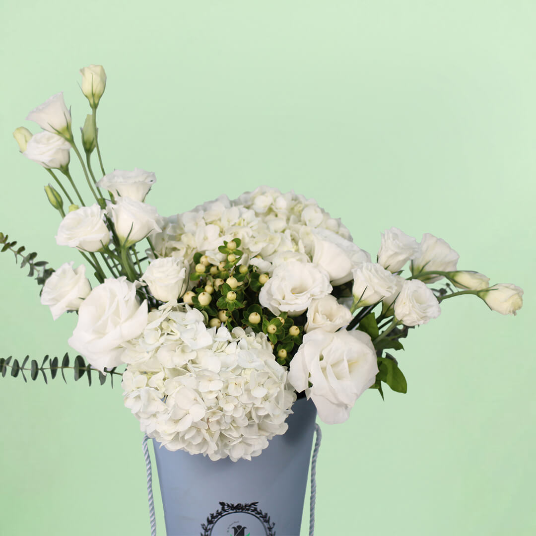 White Hydrangeas and Eustoma with berries and greenery arranged in a tall blue flower bag.