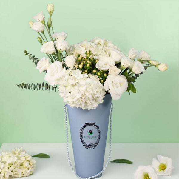 White Hydrangeas and Eustoma with berries and greenery arranged in a tall blue flower bag.
