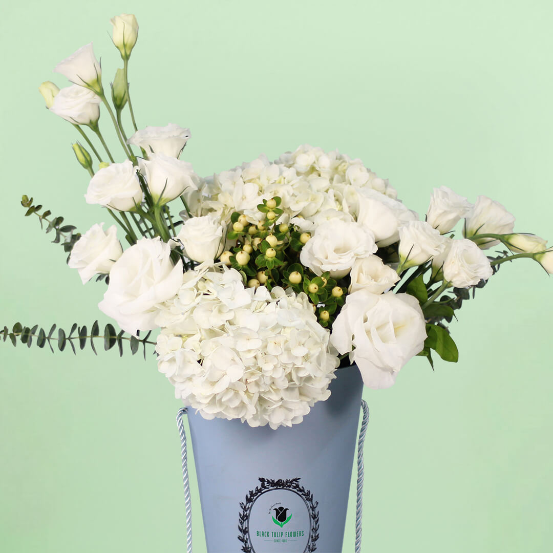White Hydrangeas and Eustoma with berries and greenery arranged in a tall blue flower bag.