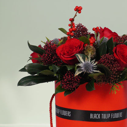 Round box Christmas flower arrangement featuring 17 to 20 roses, Ilex, Skimmia, Eryngium and Scabiosa