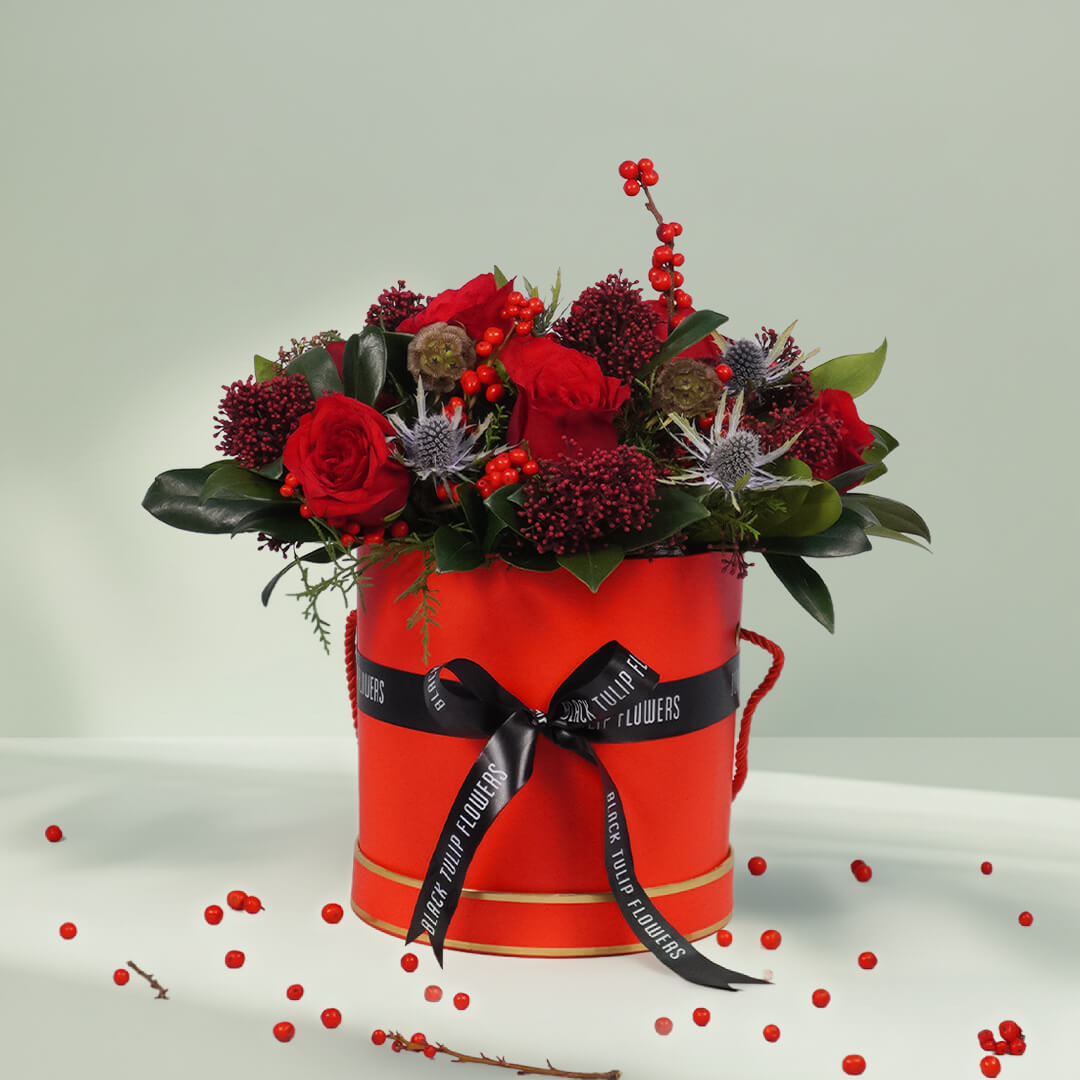Round box Christmas flower arrangement featuring 17 to 20 roses, Ilex, Skimmia, Eryngium and Scabiosa