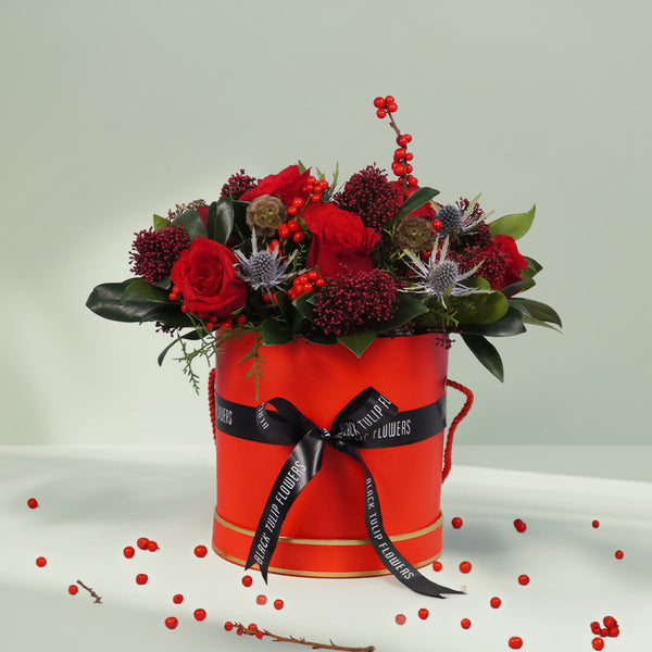 Round box Christmas flower arrangement featuring 17 to 20 roses, Ilex, Skimmia, Eryngium and Scabiosa
