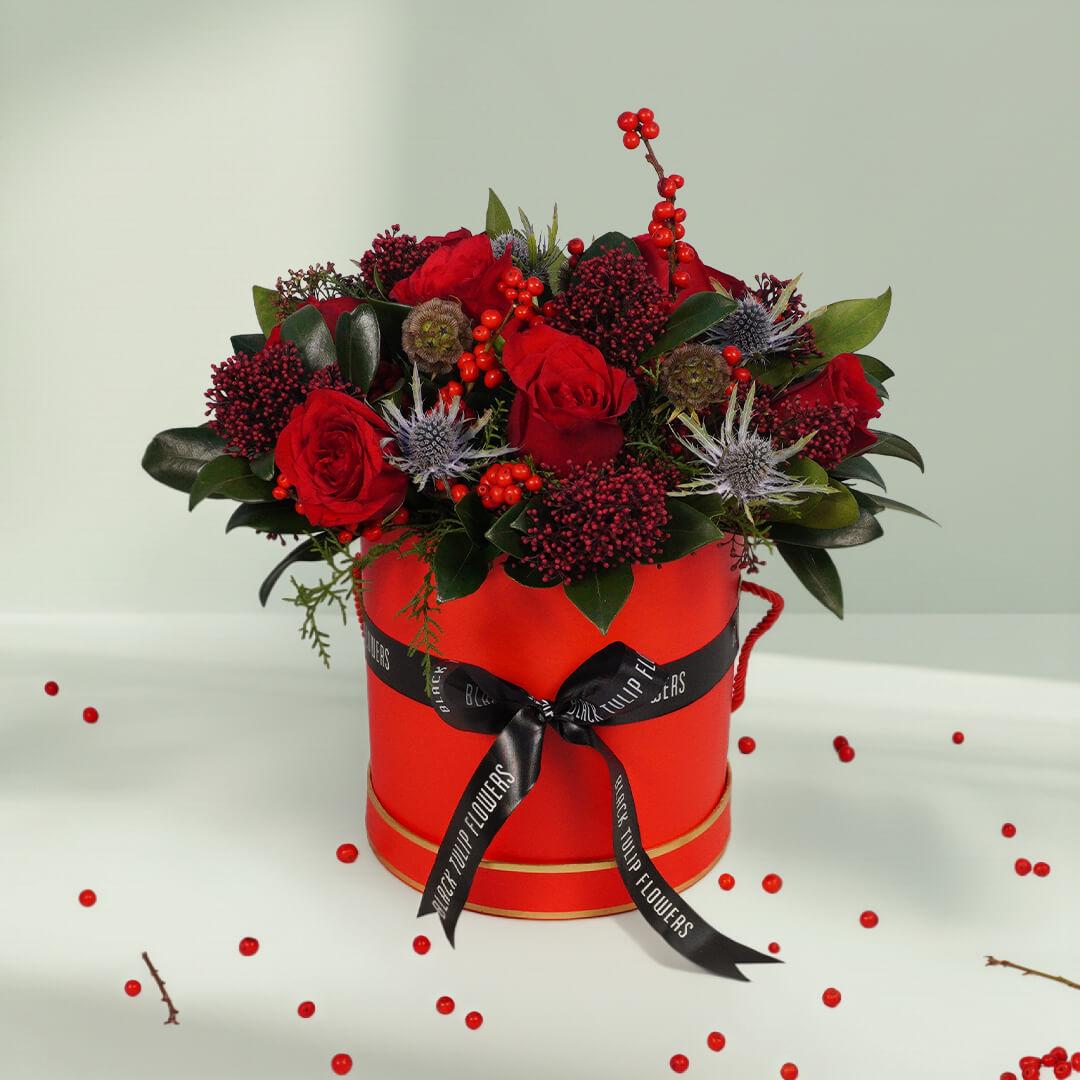Round box Christmas flower arrangement featuring 17 to 20 roses, Ilex, Skimmia, Eryngium and Scabiosa