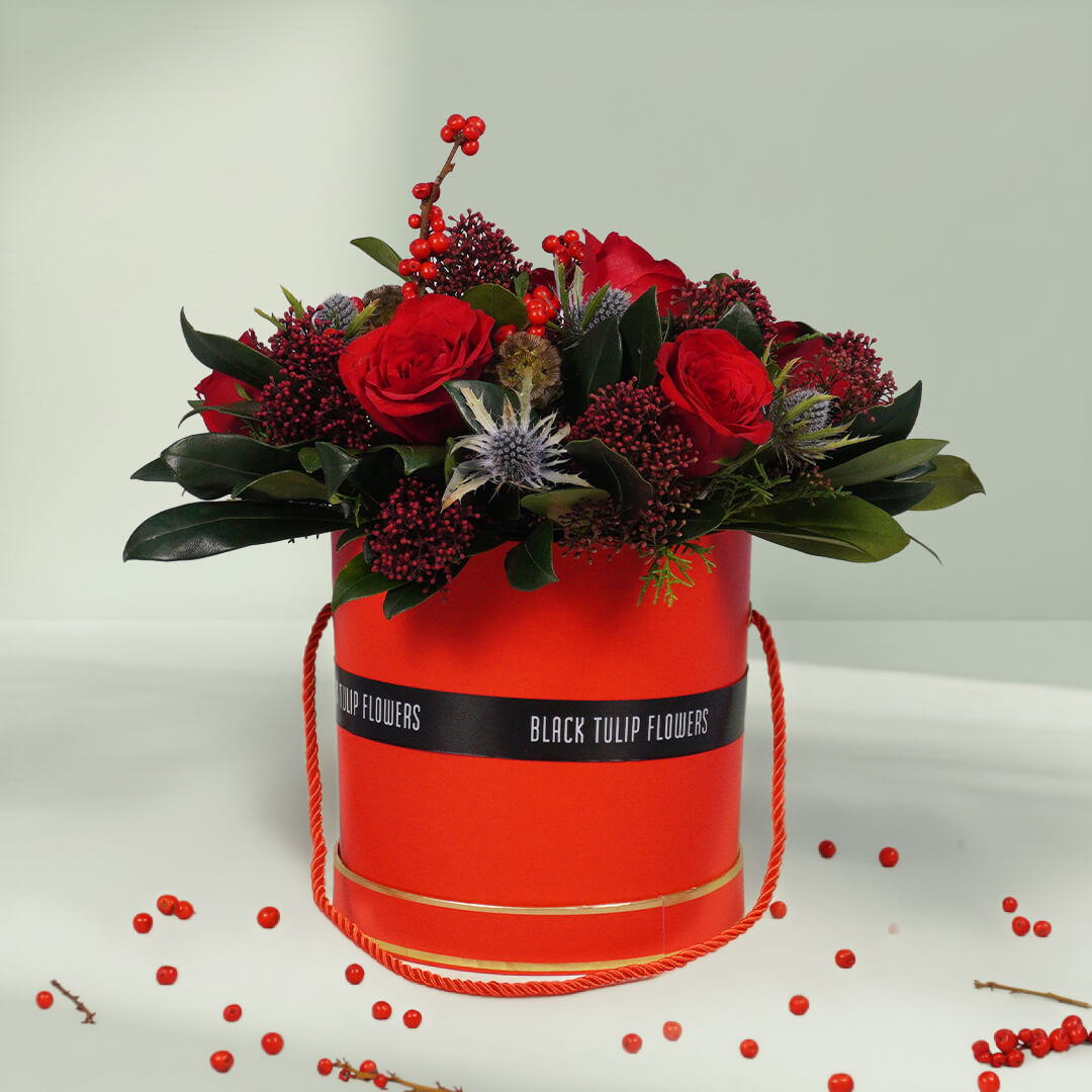 Round box Christmas flower arrangement featuring 17 to 20 roses, Ilex, Skimmia, Eryngium and Scabiosa