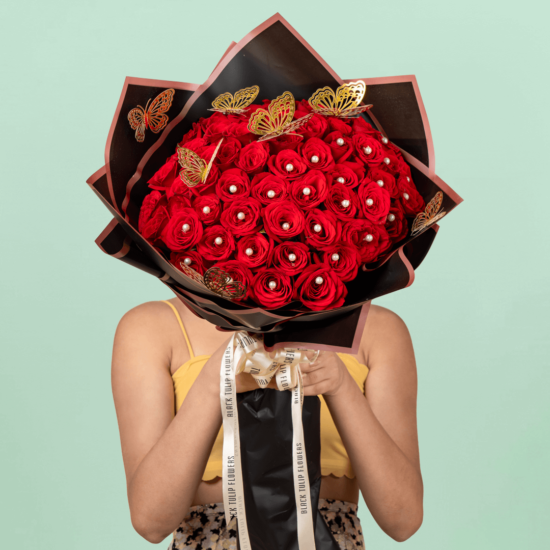 Love bouquet with 50 red roses, pearl accents, and butterfly sticker in black wrap.