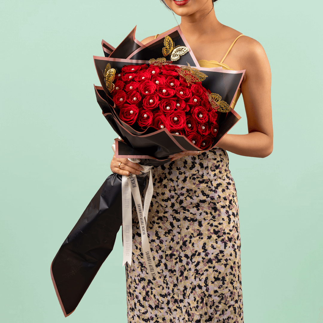 Love bouquet with 50 red roses, pearl accents, and butterfly sticker in black wrap.