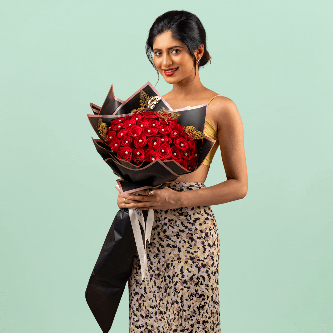 Love bouquet with 50 red roses, pearl accents, and butterfly sticker in black wrap.