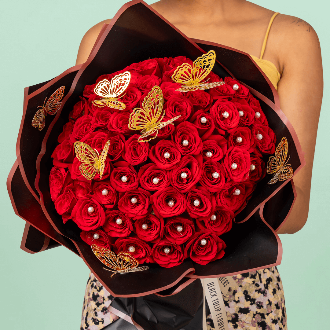 Love bouquet with 50 red roses, pearl accents, and butterfly sticker in black wrap.