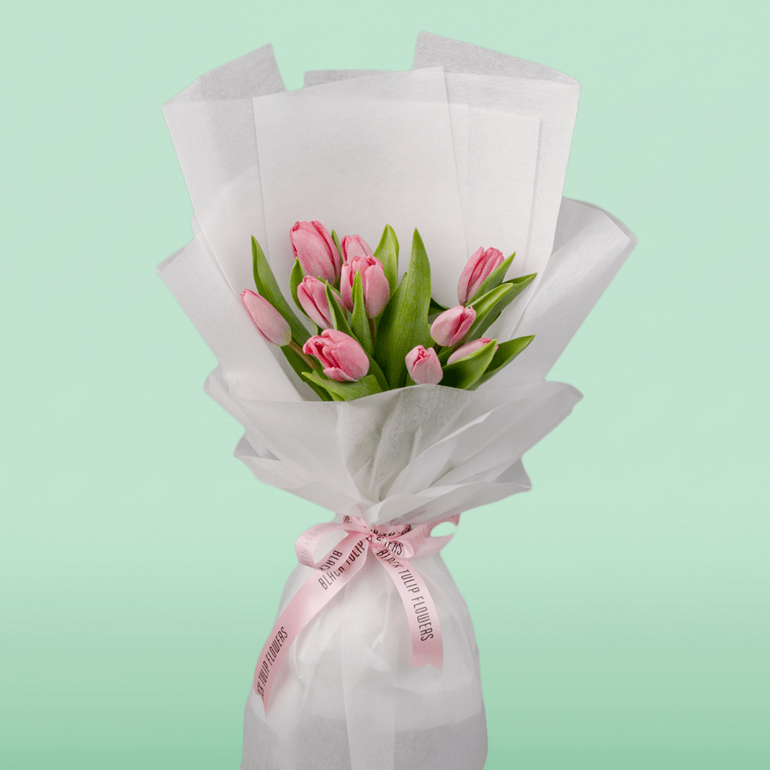 Bouquet of 10 pink Tulips with green leaves wrapped in white non-woven paper.