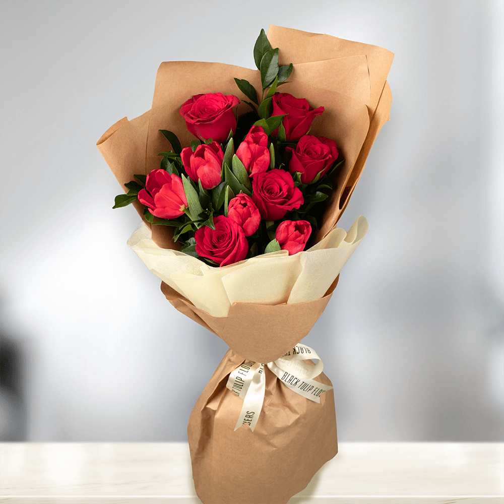 Red Tulips and Roses with greenery wrapped in brown non-woven paper.