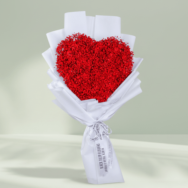 Heart shaped red flower bouquet arranged in white wrapping and finished with a ribbon.