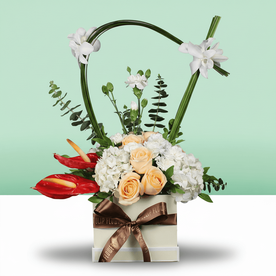 A small white square box of peach roses, white hydrangea, Eustoma, snapdragons, and steel grass.
