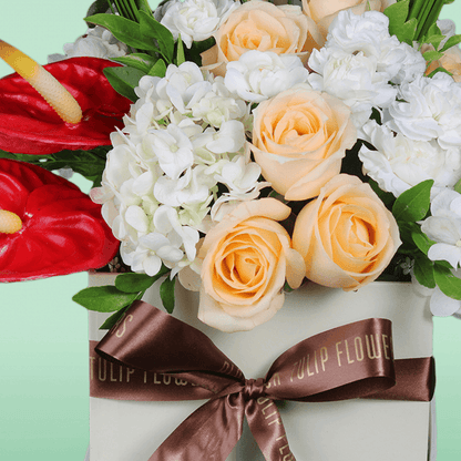 A small white square box of peach roses, white hydrangea, Eustoma, snapdragons, and steel grass.
