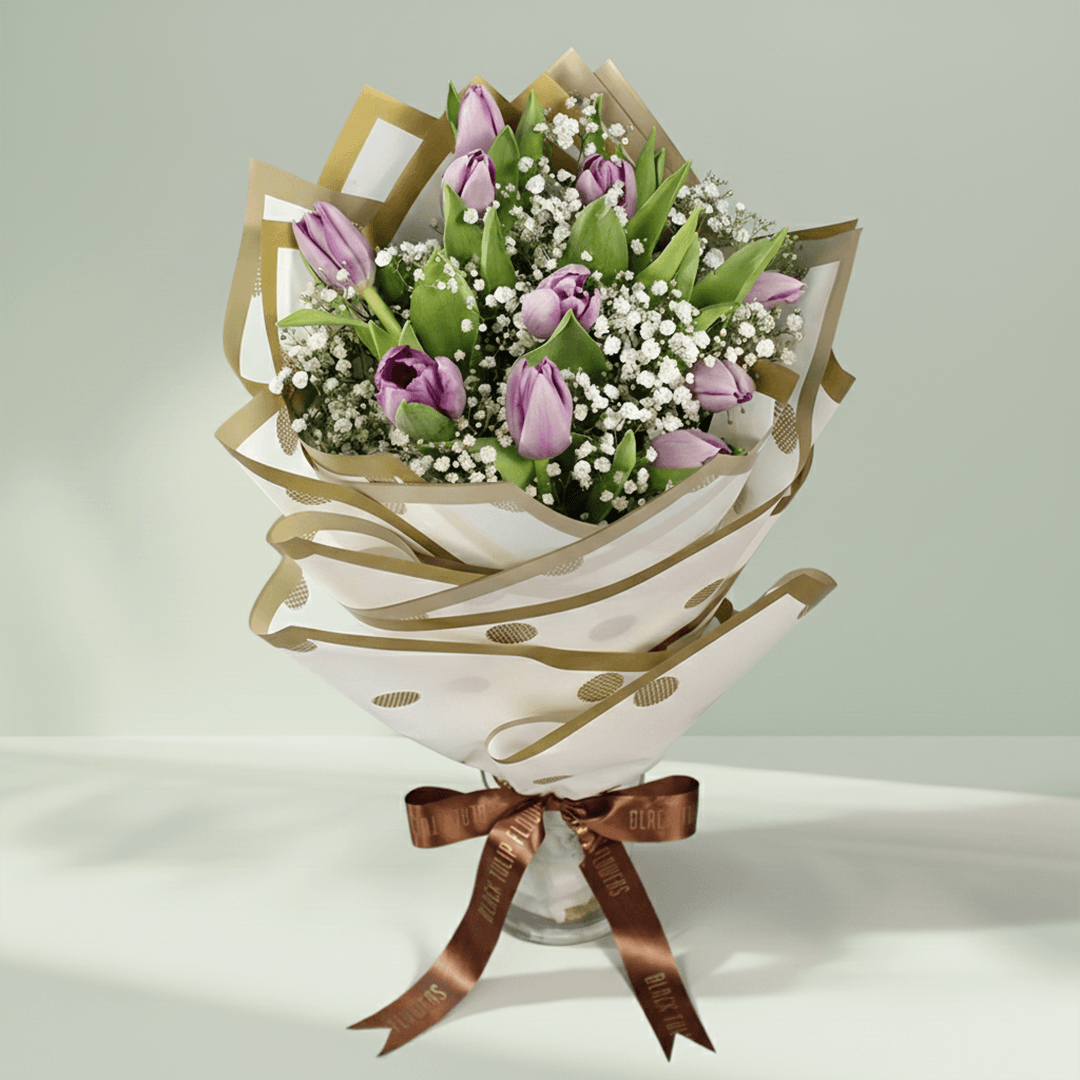 Purple tulip bouquet with baby’s breath, green foliage and elegant gold-accented wrapping.