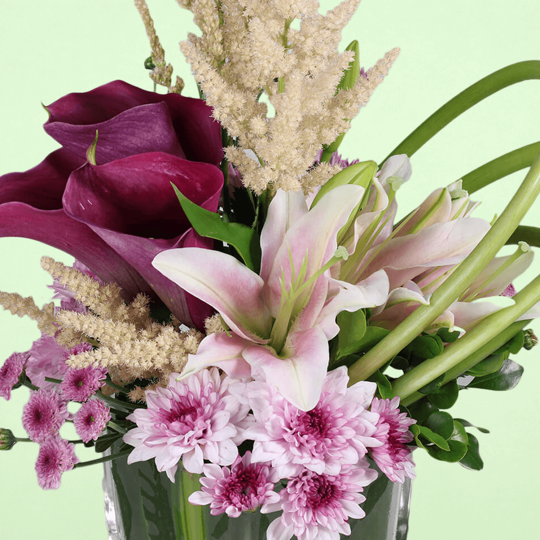 A square glass vase arrangement of calla lilies, astilbe, lilies and chrysanthemums.

