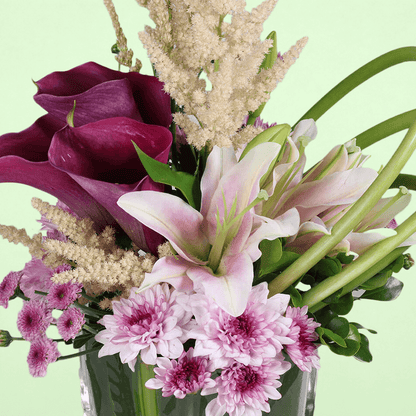A square glass vase arrangement of calla lilies, astilbe, lilies and chrysanthemums.
