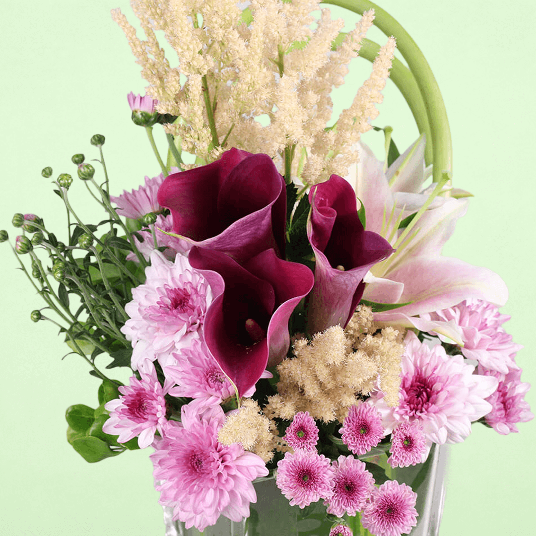 A square glass vase arrangement of calla lilies, astilbe, lilies and chrysanthemums.
