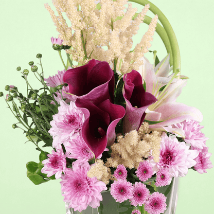 A square glass vase arrangement of calla lilies, astilbe, lilies and chrysanthemums.
