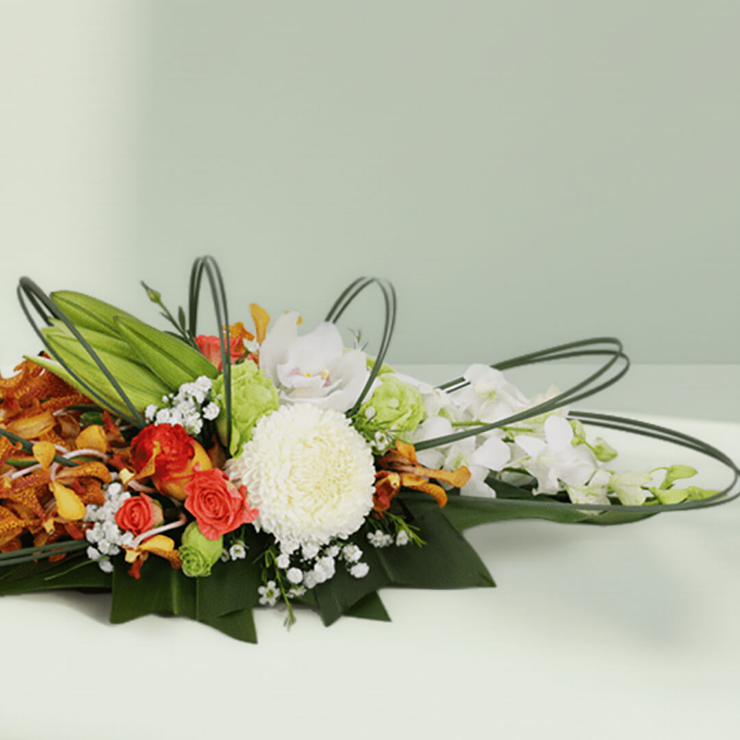 Orange orchids, white chrysanthemums and roses arranged with curved greenery on a long green tray

